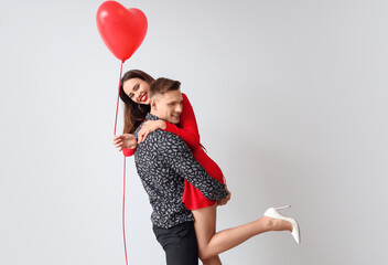 Happy young couple with balloon on light background. Valentine's Day celebration