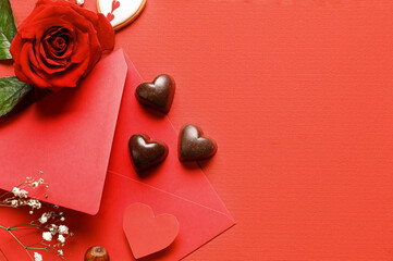 Tasty heart-shaped candies with envelope and rose on red background