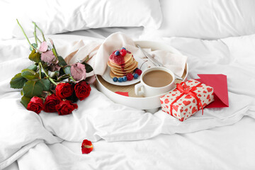 Fototapeta na wymiar Tray with tasty breakfast, bouquet of roses and gift box for Valentine's Day on bed