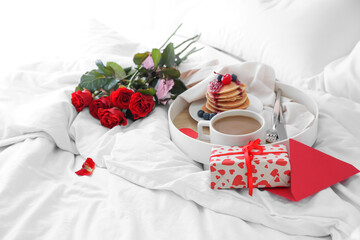 Tray with tasty breakfast, bouquet of roses and gift box for Valentine's Day on bed