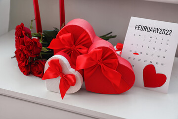 Gifts, rose flowers and calendar with marked date of Valentine's Day on table in room