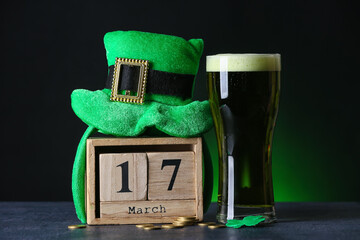 Leprechaun's hat, glass of beer and calendar on table against dark background. St. Patrick's Day celebration