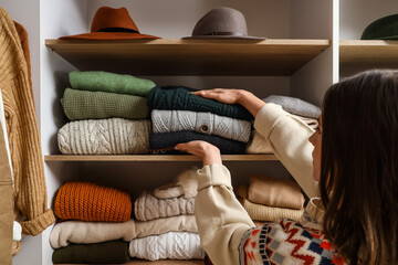 Woman taking warm sweaters from shelf in wardrobe, closeup