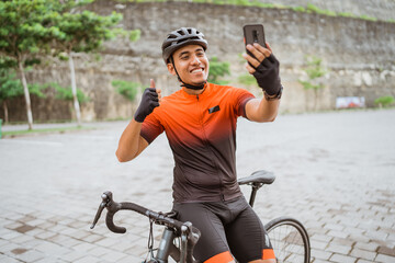 male cyclist sitting on bike and using phone to take selfie or video calling