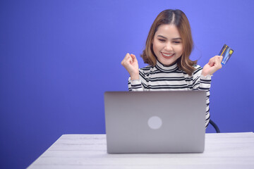 Happy young woman is shopping online via laptob , holding credit card.