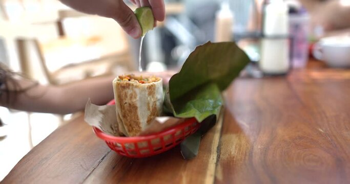 Hand squeezing lime onto tasty burritos on wooden table
