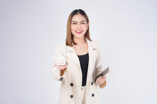 Young Beautiful Woman In Suit Holding Small Model House Over White Background Studio