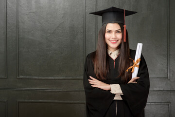 Portrait of young woman in graduation gown smiling and cheering on black background