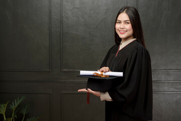 Portrait of young woman in graduation gown smiling and cheering on black background