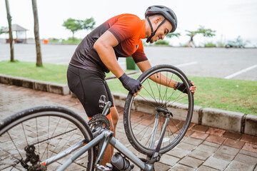 asian male cyclist checking his road bike tire