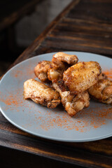 Spicy fried chicken wings in a plate on a wooden table sprinkled with spices. Vertical orientation, copy space, no people