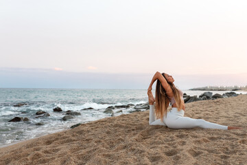 Young flexible caucasian woman practicing yoga on the beach at sunset. Copy space.