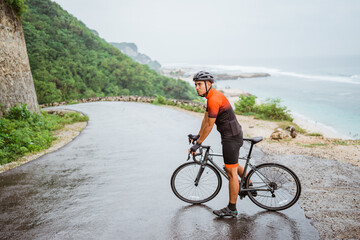 Fototapeta premium male asian cyclist with red and black jersey standing on his bike