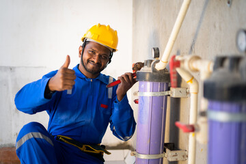 smilling young indian engineer or repairman showing thumbs up sign or hand gesture while working at...