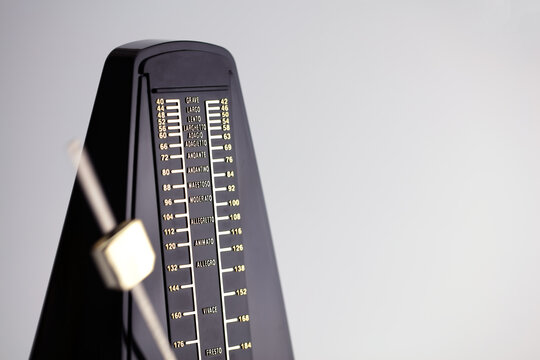 A pendulum type metronome with pendulum in motion. On neutral white background