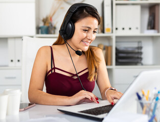 Naklejka premium Young woman call centre operator with headphones working in modern office