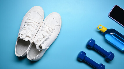Sneakers, dumbbells, smart phone and bottle of water on blue background.