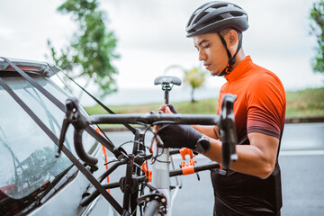 Male cyclist unloading his bicycle on a rack of his car
