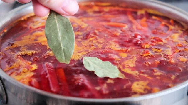 Cooking Russian beetroot soup borsch in red saucepan. 