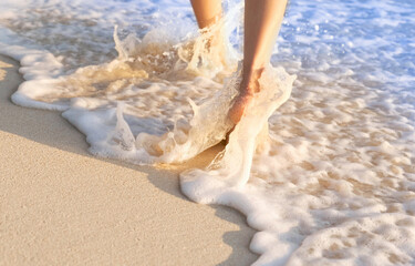 Fototapeta na wymiar woman walking to sea and beach on a beautiful island Ocean foam wrapped around a girl's leg. Walking in the early morning sunshine to get natural vitamin D