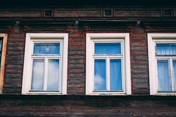 The wall of an old wooden house with red wooden boards and white windows on a sunny day.