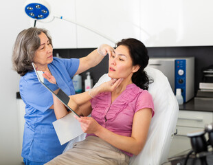 Skillful mature cosmetologist consulting woman in medical esthetic office
