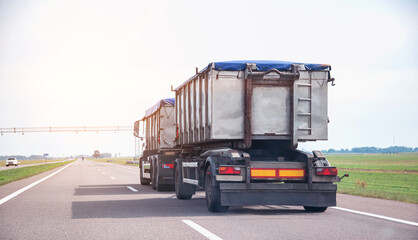 Transportation of grain in a dump truck with a trailer covered with an awning on the road. Agribusiness, copy space for text © HENADZY