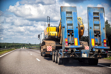Transporting a heavy excavator in a truck trailer. Highway heavy oversized cargo transportation, industry. Copy space for text