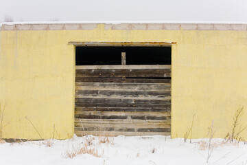 The facade of a small yellow one-story building, the entrance of which is closed with boards.