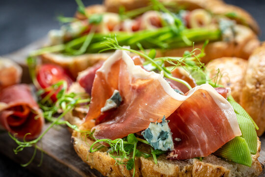 Variety of aperitifs Croissant sandwiches with jamon ham serrano paleta iberica, blue cheese, avocado, microgin on blue background. Delicious snack, appetizers, tapas