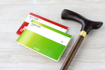 老後・介護の金銭的な備えイメージ―レプリカの通帳と高齢者用の杖