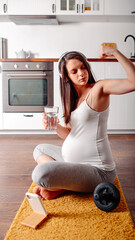 Pregnant doing workout on orange fitness mat. Pragnant yoga at home in the kitchen. Pregnant in white headphones.