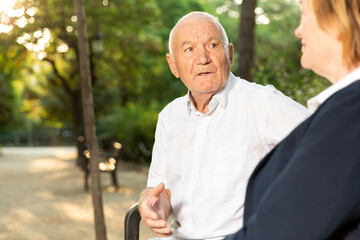 Happy senior man and woman having conversation on bench in green park