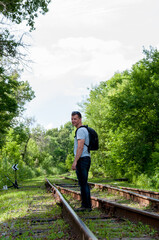 Fototapeta na wymiar A man with a backpack stands on the rails of a railway in the summer