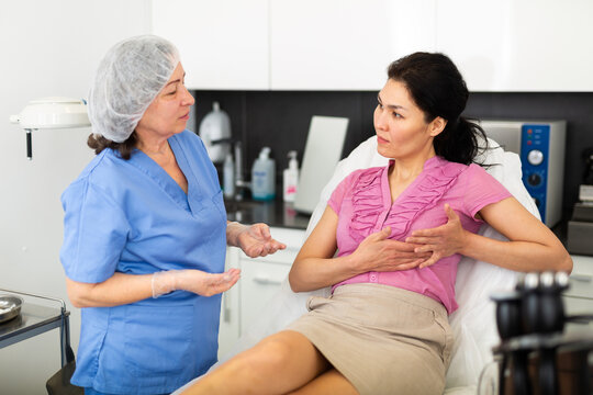 Plastic surgeon and woman discussing procedure of breast augmentation during consultation at clinic