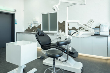 Black leather armchair for patients of modern dental clinics standing in the center of office surrounded by medical equipment