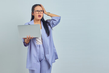 Portrait of surprised young Asian woman standing using laptop and holding head with palms isolated over white background