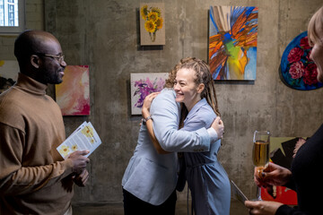 Happy young female embracing modern artist while standing against wall with collection of his...