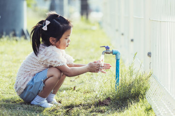 Cute 5 year old kid girl is washing her two hands from water tap. Child rubs hands together to wash...