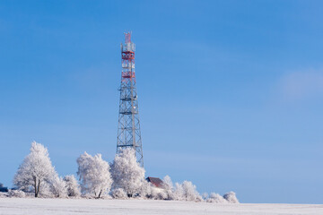 Transmission tower in winter, Telecommunications tower with cellular antenna and satellite dish