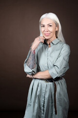 Portrait of mature woman with tattoo in her hand posing at camera in elegant dress against the...