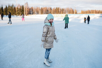Children's skating on an outdoor ice rink, a little happy girl learns to skate, winter sports and outdoor entertainment.