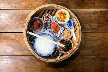 Chinese Porridge served with various side dishes on steamed bowl on a wooden background
