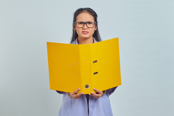 Portrait of pensive young Asian business woman holding yellow folder isolated on purple background