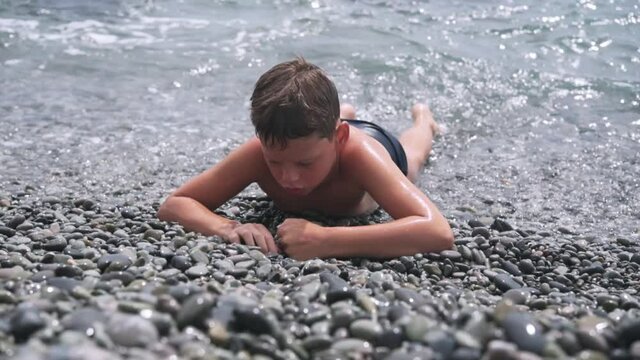 A boy lying on the pebbe beach with foamy sea waves hitting the pebble seashore behind him