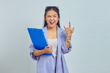 Portrait of emotional young Asian business woman in suit holding document folder and making rock...