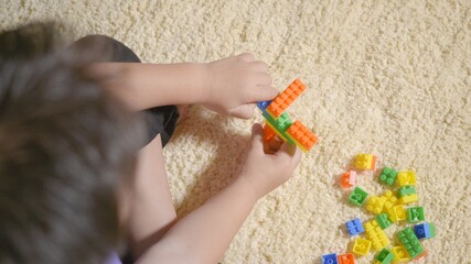 Happy Asian kid boy preschool playing creative plastic toy blocks staying at home. Funny little child sitting building tower of colorful block, Educational construction game concept