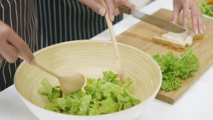 Happy Asian beautiful family couple husband and wife cooking vegetable salad in kitchen together at home. The man mix the vegetables in a cup woman sliced bread. healthy food concept,