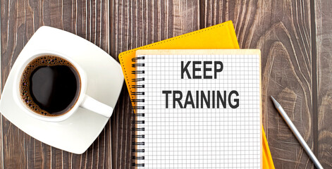KEEP TRAINING text on the notebook with coffee on wooden background