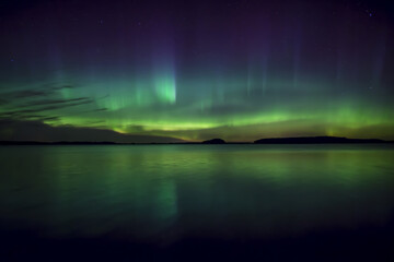 Northern lights dancing over calm lake in north of Sweden.
